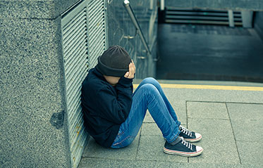 Vergrößerungsansichten für Bild: Ein Kind sitzt verzweifelt an eine Mauer gelehnt und versteckt sein Gesicht hinter den Händen